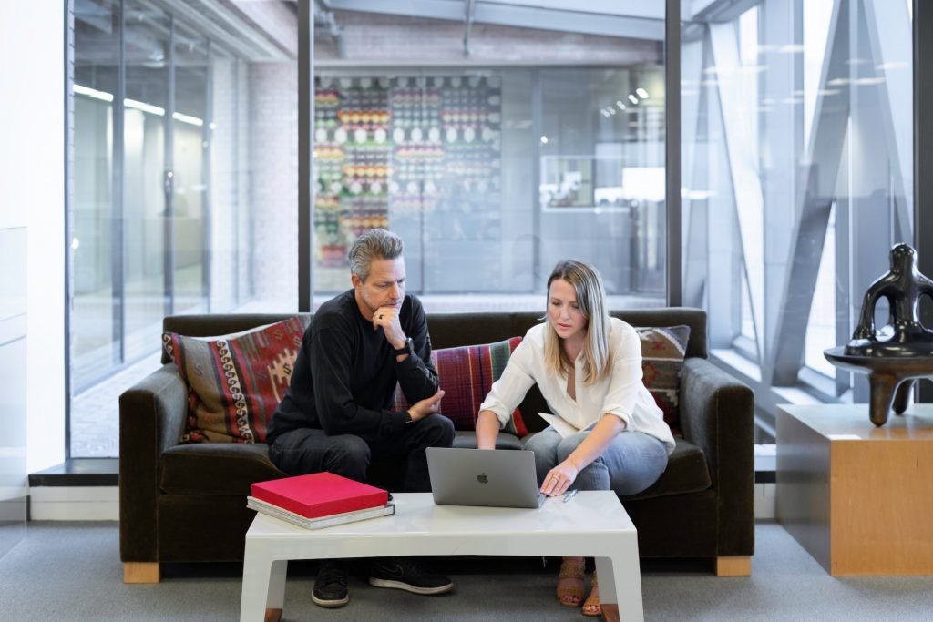 Woman and man sales meeting sitting on sofa glass wall behind modern office